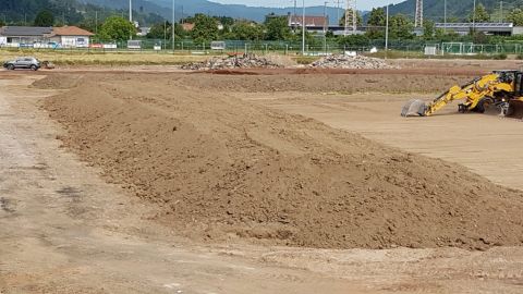 Hinten sind Berge von Asphalt und Betonplatten, davor die rote Erde. Der aufgehäufte Mutterboden um das Spielfeld wird wieder aufgebracht